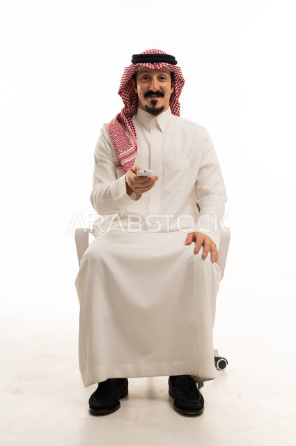 رجل سعودي يمسك جهاز تحكم عن بعد بخلفية بيضاء