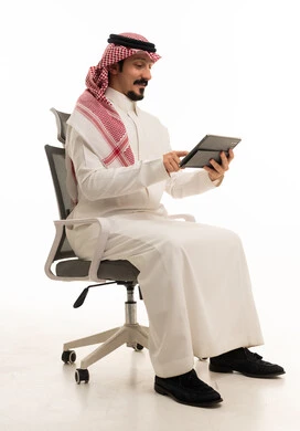 رجل سعودي يستخدم جهاز لوحي رقمي على كرسي مكتب بخلفية بيضاء