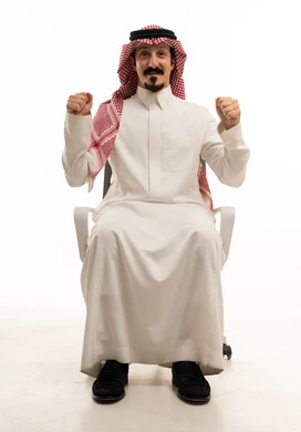 رجل سعودي يجلس على كرسي مكتب ويحتفل بالنجاح