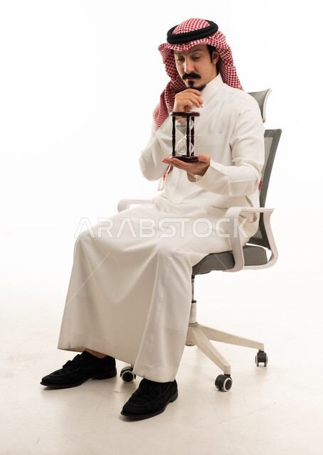رجل سعودي يحمل ساعة رملية على كرسي مكتب
