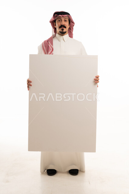 رجل سعودي يحمل لوحة بيضاء فارغة بخلفية استوديو