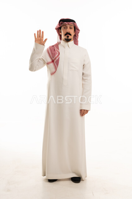 رجل سعودي بالزي التقليدي يرفع يده على خلفية بيضاء