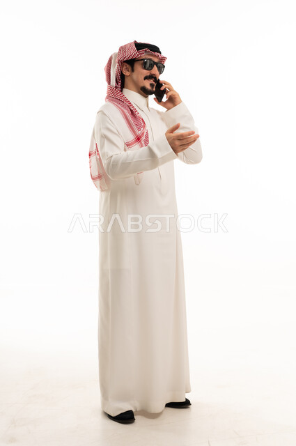 رجل سعودي بالثوب يتحدث في الجوال بخلفية بيضاء