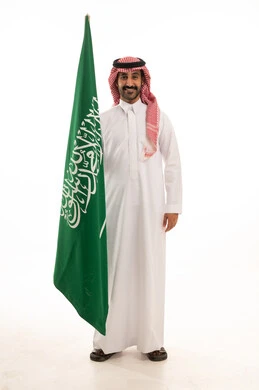 رجل سعودي يحمل علم المملكة العربية السعودية بالزي التقليدي