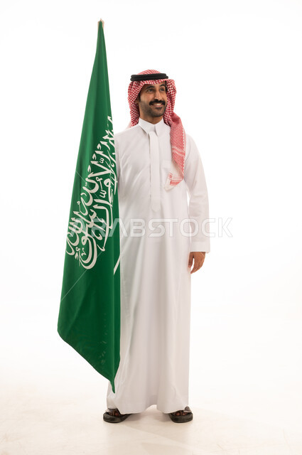 رجل سعودي بالثوب والشماغ يقف بجانب العلم