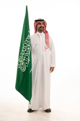 رجل سعودي بالثوب والشماغ يقف بجانب العلم
