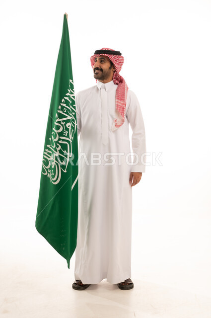 رجل سعودي بالزي التقليدي يمسك علم السعودية