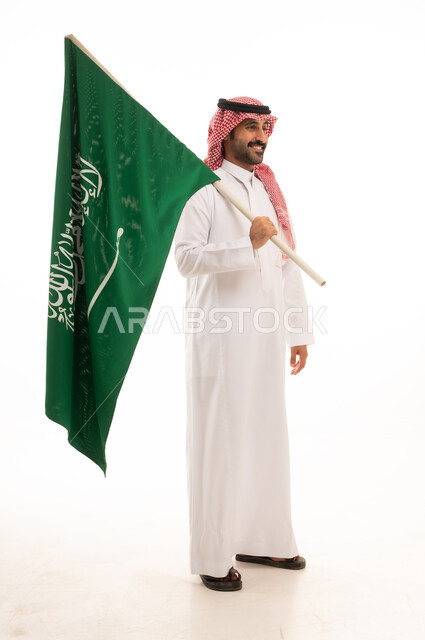 رجل سعودي بالثوب التقليدي يحمل علم المملكة