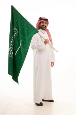 رجل سعودي بالزي التقليدي يحمل علم المملكة العربية السعودية