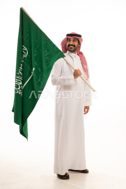 رجل سعودي بالثوب والشماغ يحمل العلم الوطني