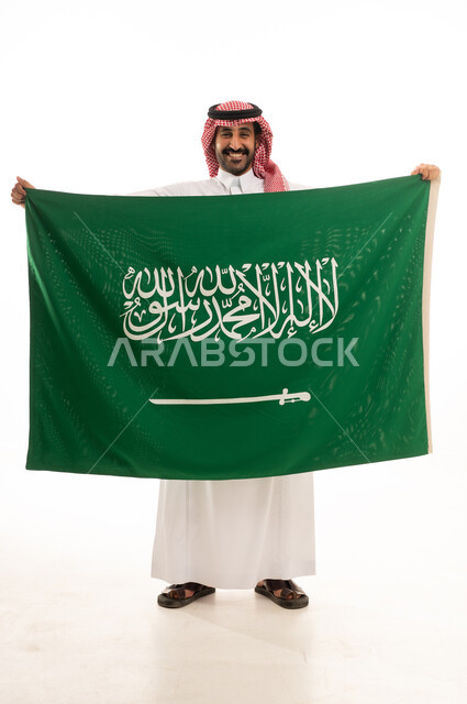 رجل سعودي بالزي التقليدي يرفع علم المملكة العربية السعودية