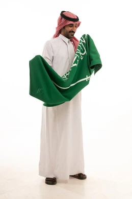 رجل سعودي بالزي التقليدي يمسك علم المملكة العربية السعودية