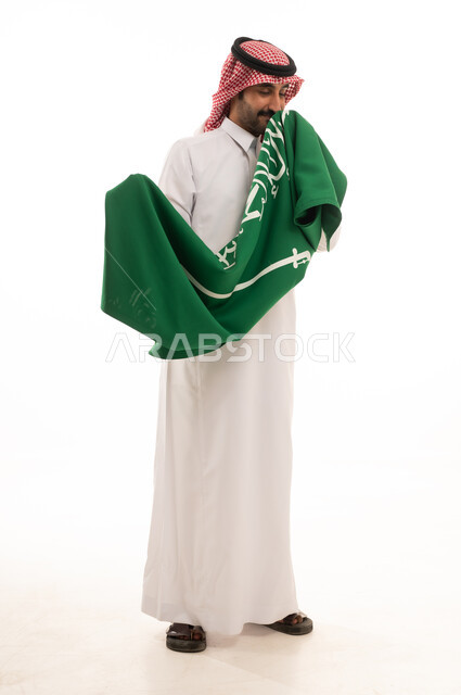 رجل سعودي بالزي التقليدي يمسك علم المملكة