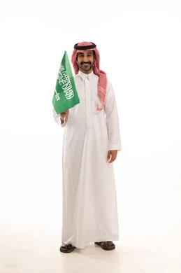 رجل سعودي بالثوب التقليدي يحمل علم السعودية