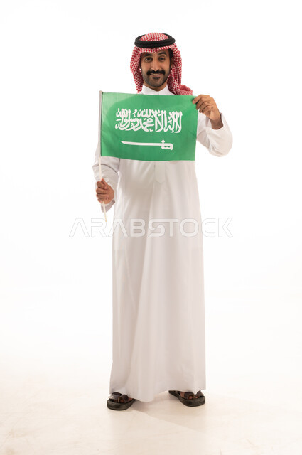 رجل سعودي بالزي التقليدي يرفع علم المملكة