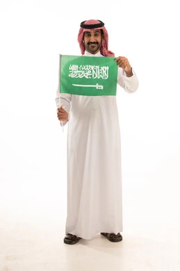 رجل سعودي بالزي التقليدي يرفع علم المملكة