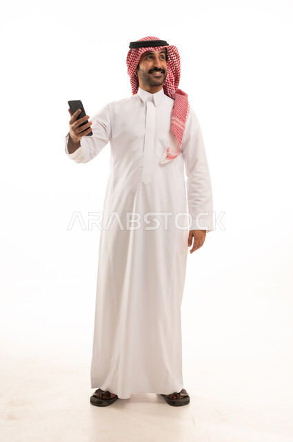 رجل سعودي بالثوب والشماغ يحمل هاتف ذكي في الاستوديو