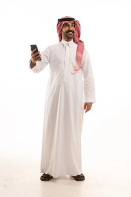 رجل سعودي بالثوب والشماغ يحمل هاتف ذكي في الاستوديو