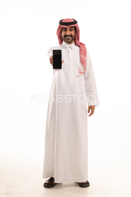 رجل سعودي بالثوب يمسك هاتفاً ذكياً بخلفية بيضاء