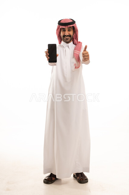 رجل سعودي بالثوب يمسك هاتف ذكي مع إشارة الإبهام