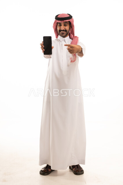 رجل سعودي بالثوب يمسك ويشير إلى هاتف ذكي