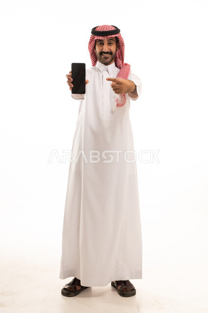 رجل سعودي بالثوب والشماغ يمسك هاتف ذكي