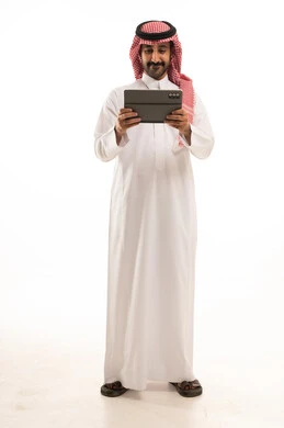 رجل سعودي بالثوب والشماغ يستخدم جهاز لوحي خلفية بيضاء
