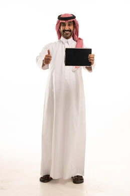 رجل سعودي بالثوب والشماغ يحمل جهاز لوحي وإيماءة نجاح