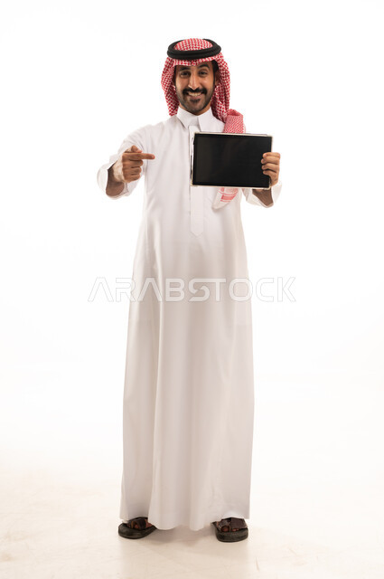 رجل سعودي بالثوب يشير إلى جهاز لوحي رقمي