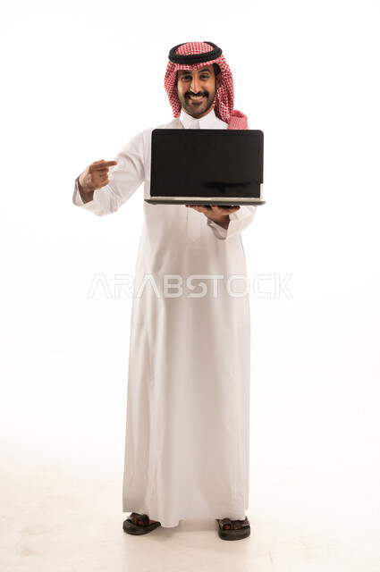 رجل سعودي بالثوب والشماغ يشير إلى شاشة لابتوب