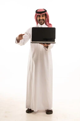 رجل سعودي بالثوب والشماغ يشير إلى شاشة لابتوب