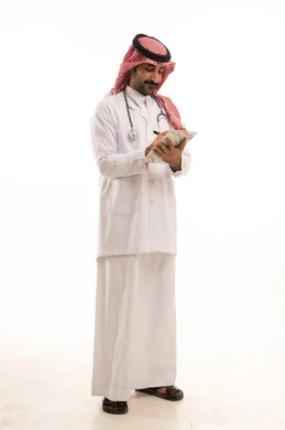 Saudi Male Doctor in Traditional Thobe Writing on Clipboard Saudi Male Doctor in Traditional Thobe Writing on Clipboard