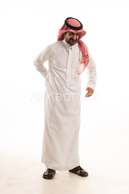 آلام العامود الفقري والظهر، بورتريه لرجل عربي خليجي سعودي يرتدي الشماغ والثوب التقليدي منحني يضع يده على ظهره، إيماءات وتعابير جسد تدل على الوجع والألم، التعب والإرهاق والإحساس بالمرض، الحاجة إلى العلاج وزيارة الطبيب، صورة الجسم بالكامل، خلفية بيضاء