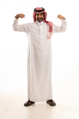 Bodybuilding, fitness for athletes, building a sporty body, a portrait of an Arab Gulf Saudi man wearing traditional attire and a ghutrah raising his arm muscles, a full-body image, white background.