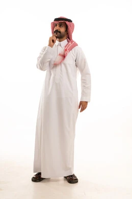 تعابير شرود الذهن والتمعن، ايجاد حل لمشكلة ما، التأمل والتخطيط للمستقبل، بورتريه لرجل عربي خليجي  سعودي يرتدي الزي التقليدي والشماغ يضع يده على ذقنه بايماءات التفكير والتركيز، صورة لكامل الجسم، خلفية بيضاء