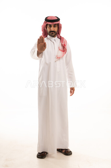 الصمت والتوقف عن الكلام, الأمر بالنهي عن فعل شيء ما, بورتريه لرجل عربي خليجي سعودي يرتدي الثوب والشماغ التقليدي يرفع كفه للأعلى, طلب خفض الصوت والتهديد, صورة لكامل الجسم, خلفية بيضاء