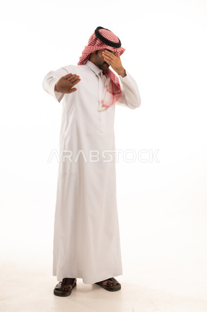 الصمت والتوقف عن الكلام, الأمر بالنهي عن فعل شيء ما, بورتريه لرجل عربي خليجي سعودي يرتدي الثوب والشماغ التقليدي يرفع كفه للأعلى, طلب خفض الصوت والتهديد, صورة لكامل الجسم, خلفية بيضاء