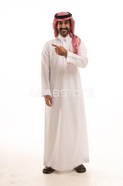 الإشارة إلى شيء ما, الوقوف باستقامة واعتدال, بورتريه لرجل عربي خليجي سعودي  يرتدي الزي التقليدي والشماغ يشير بيديه لمكان معين, صورة للجسم بالطول الكامل, خلفية بيضاء