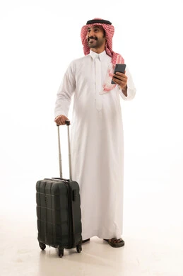 الاستعداد لقضاء رحلة صيفية ممتعة، مفهوم السياحة في إجازة الصيف، القيام بالجولات الترفيهية، بورتريه لرجل عربي خليجي سعودي يرتدي الزي التقليدي والشماغ يحمل بيده هاتف محمول وشنطة سفر بتعابير السرور، خلفية بيضاء