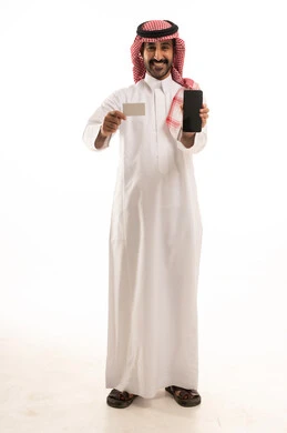 استخدام التقنيات الحديثة، بورتريه لرجل عربي خليجي سعودي يرتدي الثوب التقليدي والشماغ يستخدم الهاتف والبطاقة الائتمانية، خلفية بيضاء.