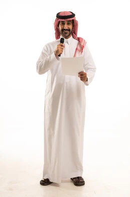 تقديم الفقرات باستخدام الميكروفون، اعداد التقارير الخاصة بالعمل، متابعة ومراجعة الخطط والمشاريع المكتبية، بورتريه لرجل عربي خليجي سعودي يرتدي الثوب التقليدي والشماغ ينظر الى الاوراق البيضاء يمسك بيده المايك، الجسم بالطول الكامل، خلفية بيضاء