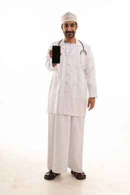 The integration of technology and technology in medicine and healthcare, working in the medical sector in the Sultanate of Oman, a portrait of an Arab Gulf Omani doctor wearing a dishdasha and kumma and the professional attire, wearing a stethoscope, using a mobile phone with expressions of joy, full-body, white background.