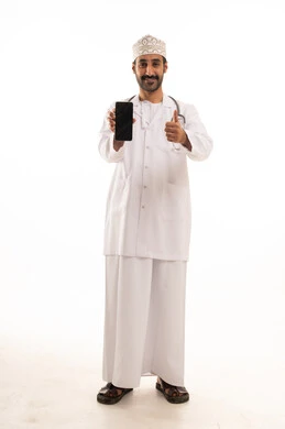 تعابير الموافقة والرضي، دمج التقنية والتكنولوجيا في الطب والرعاية الصحية، العمل في القطاع الطبي في سلطنة عمان، بورتريه لطبيب عربي خليجي عماني يرتدي الدشداشة والكمة والزي الخاص بالمهنة يضع السماعة الطبية يستخدم  الهاتف المحمول ، الجسم بالطول الكامل، خلفية بيضاء