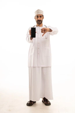 تعابير الرفض وعدم الموافقة، دمج التقنية والتكنولوجيا في الطب والرعاية الصحية، العمل في القطاع الطبي في سلطنة عمان، بورتريه لطبيب عربي خليجي عماني يرتدي الدشداشة والكمة والزي الخاص بالمهنة يضع السماعة الطبية يستخدم  الهاتف المحمول، الجسم بالطول الكامل، خلفية بيضاء