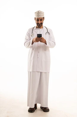 دمج التقنية والتكنولوجيا في الطب والرعاية الصحية، العمل في القطاع الطبي في سلطنة عمان، بورتريه لطبيب عربي خليجي عماني يرتدي الدشداشة والكمة والزي الخاص بالمهنة يضع السماعة الطبية يستخدم  الهاتف المحمول بتعابير السرور، الجسم بالطول الكامل، خلفية بيضاء