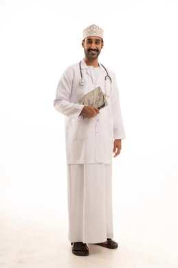العمل فى القطاع الصحي، بورتريه لطبيب عربي خليجي عماني يرتدي الدشداشة والعمامة والمعطف الطبي و الكمامة يضع السماعة الطبية يمسك بيده التقارير الطبية ، الجسم بالطول الكامل، خلفية بيضاء