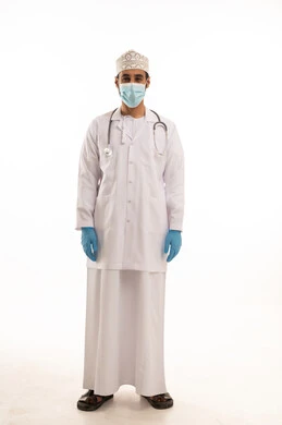 اتباع اجراءات السلامة للوقاية من فايروس كورونا،  بورتريه لطبيب عربي خليجي عماني يرتدي الدشداشة والعمامة والمعطف الطبي و الكمامة يضع السماعة الطبية يعمل في القطاع الصحي، الجسم بالطول الكامل، خلفية بيضاء