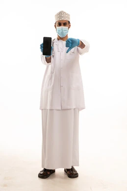 Expressions of rejection and disapproval, integrating technology and tech in medicine and healthcare, working in the medical sector in the Sultanate of Oman, a portrait of an Arab Gulf Omani doctor wearing a dishdasha and kumma and the professional attire, wearing a stethoscope and using a mobile phone, full-body, white background.