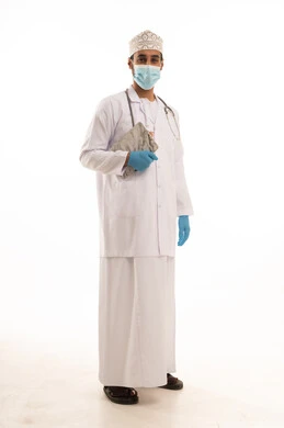 العمل فى القطاع الصحي، بورتريه لطبيب عربي خليجي عماني يرتدي الدشداشة والعمامة والمعطف الطبي و الكمامة يضع السماعة الطبية يمسك بيده التقارير الطبية ، الجسم بالطول الكامل، خلفية بيضاء