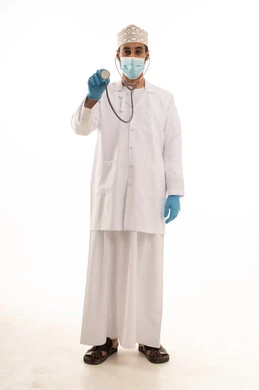 اتباع اجراءات السلامة للوقاية من فايروس كورونا،  بورتريه لطبيب عربي خليجي عماني يرتدي الدشداشة والعمامة والمعطف الطبي و الكمامة يضع السماعة الطبية يعمل في القطاع الصحي، الجسم بالطول الكامل، خلفية بيضاء